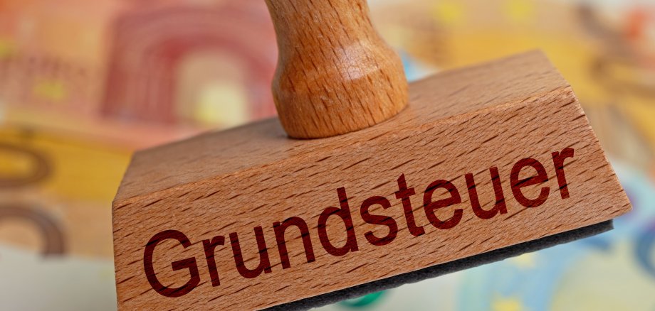 Stempel mit dem Aufdruck "Grundsteuer" vor Geldscheinen